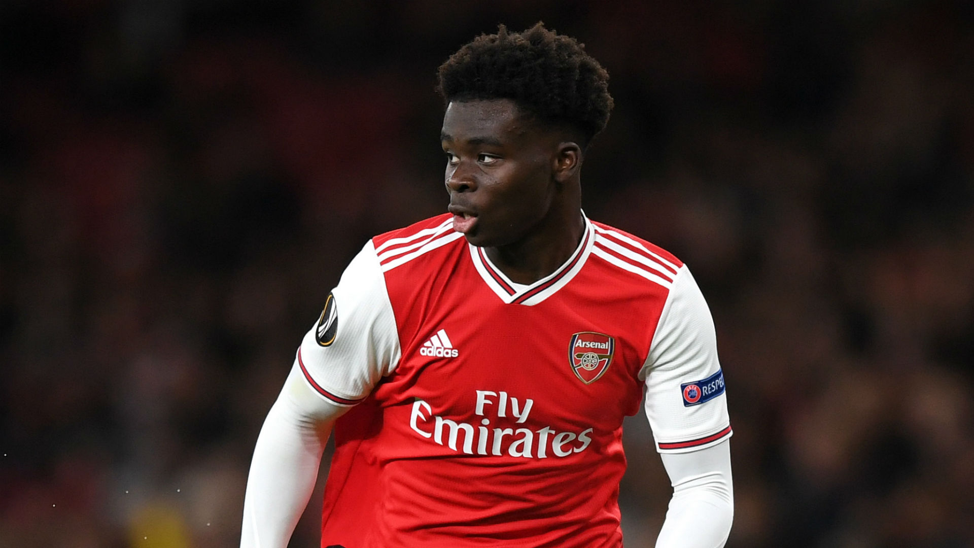  Bukayo Saka is playing soccer for Arsenal, wearing a red jersey with white sleeves and white shorts.